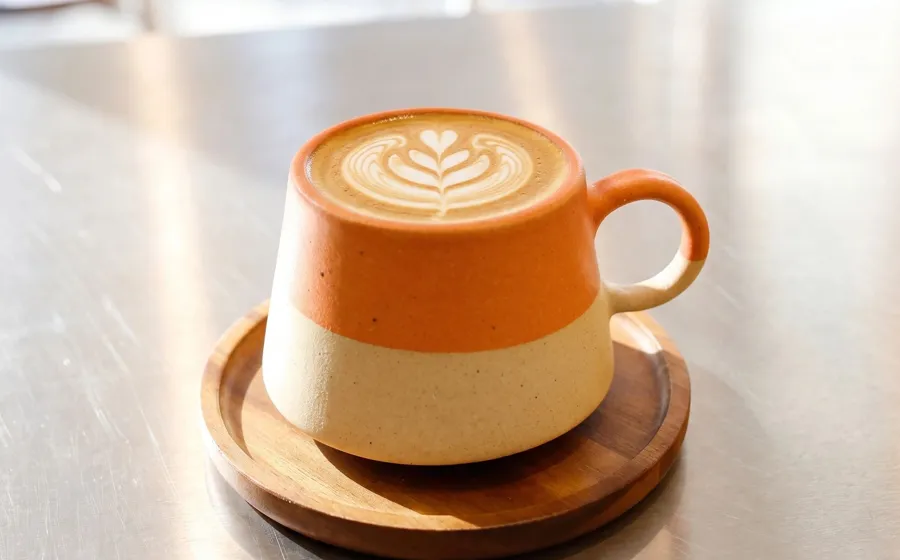 Latte con arte en una taza naranja de cerámica sobre la barra de acero de Orange Coffee.